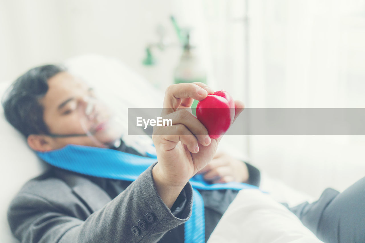 Ill man holding heart shape prop while lying on bed at hospital