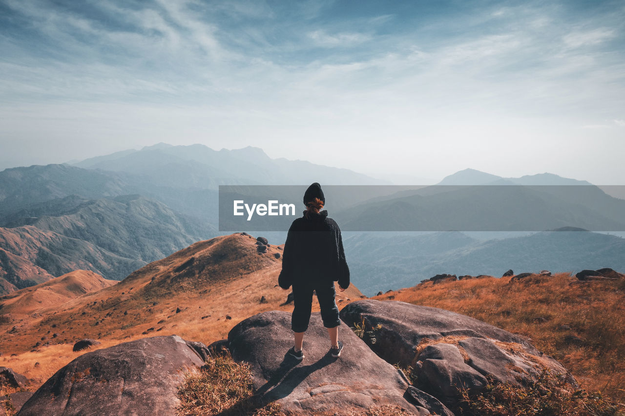 FULL LENGTH REAR VIEW OF MAN STANDING ON MOUNTAIN AGAINST SKY