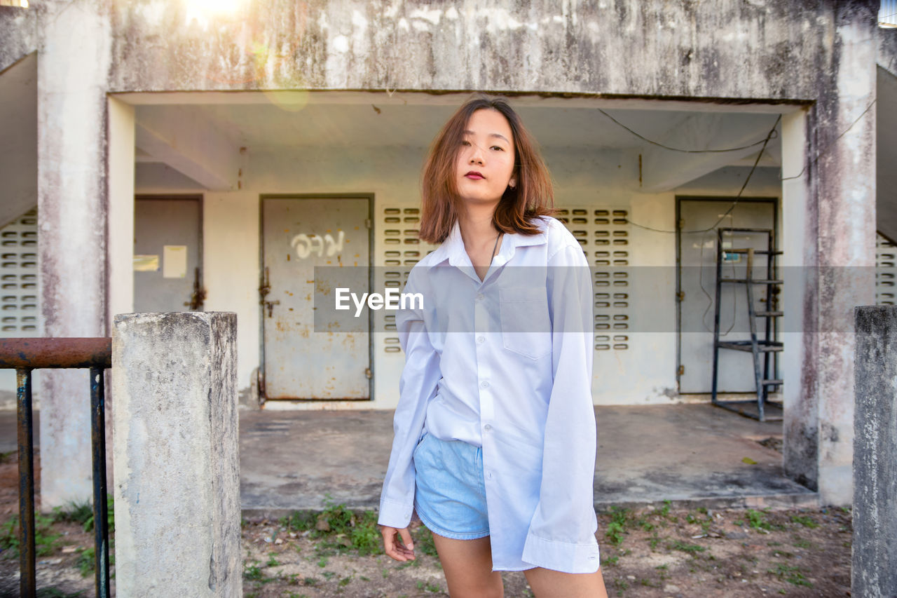 Portrait of young woman standing against building