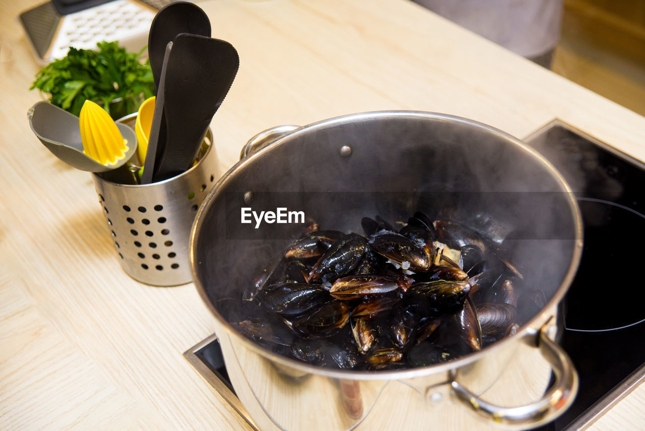 Frozen black clams are cooking in a deep pan on the stove. vapors from thawing seafood.