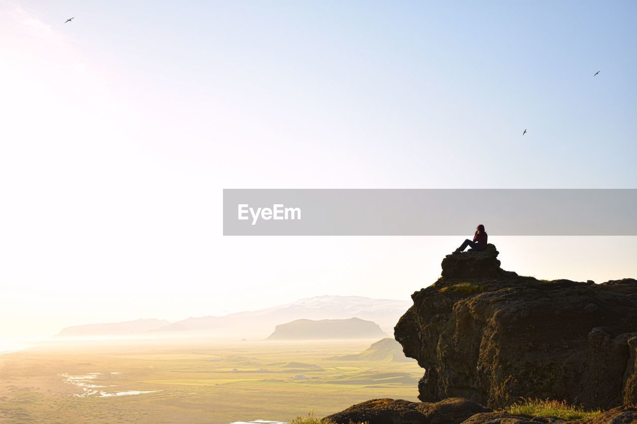 Near silhouette of woman on rock against clear sky