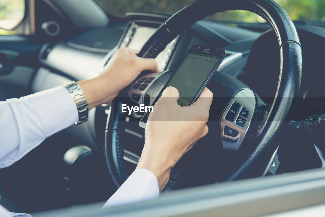 Businessman touching and using smartphone for online chat in front of steering wheel at front seat 