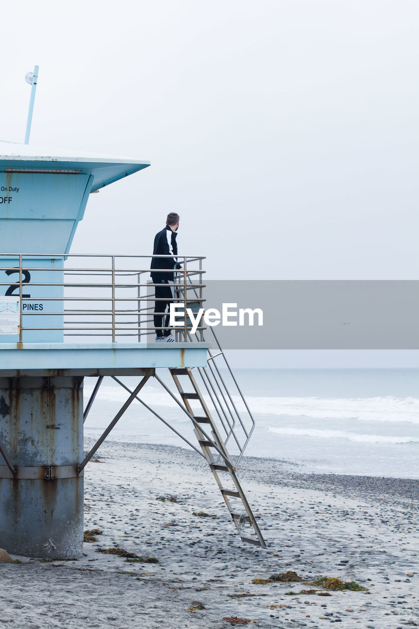 Man standing at lifeguard hut by sea against sky