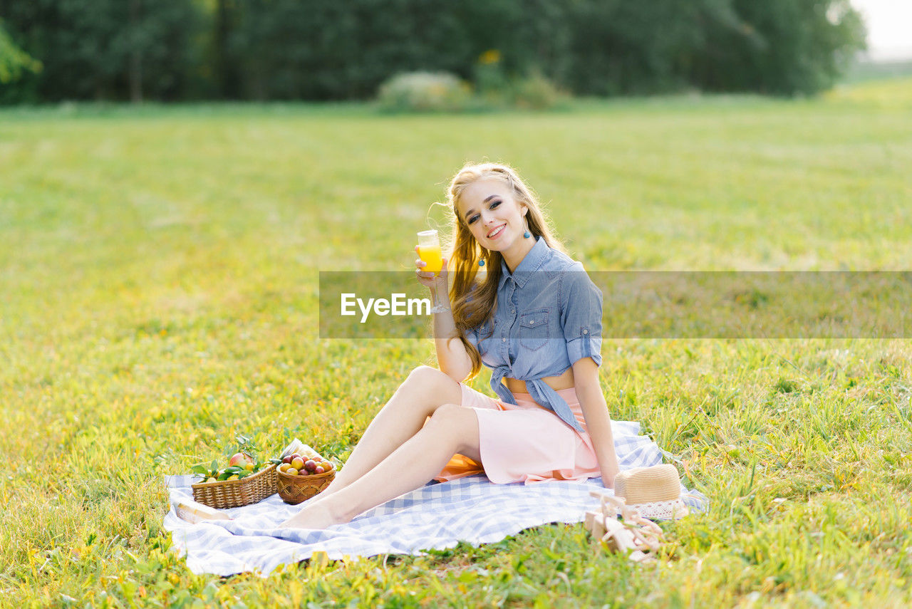 Beautiful young woman in a blue denim shirt and pink skirt in the garden at a picnic holding