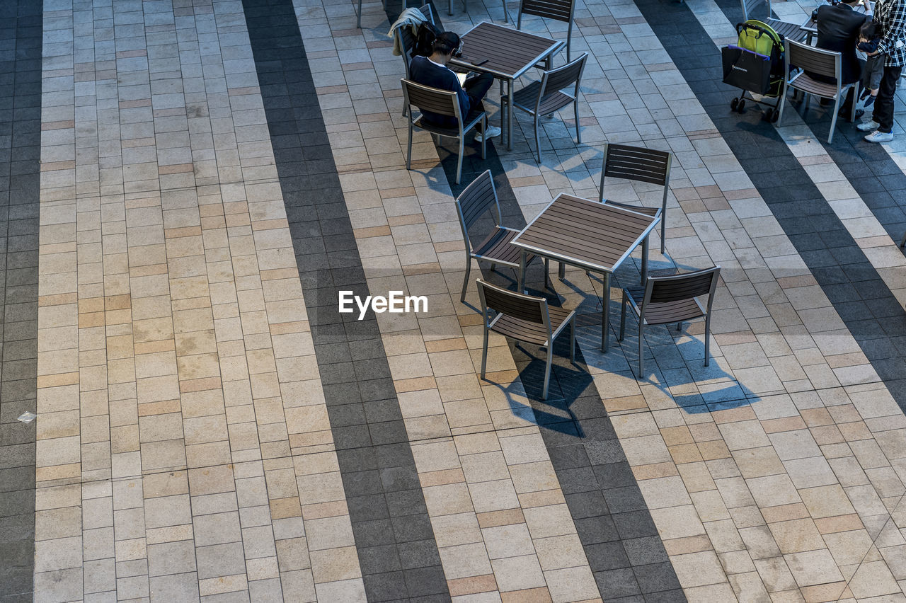 HIGH ANGLE VIEW OF CHAIRS AND TABLES AT SIDEWALK CAFE AGAINST BUILDING
