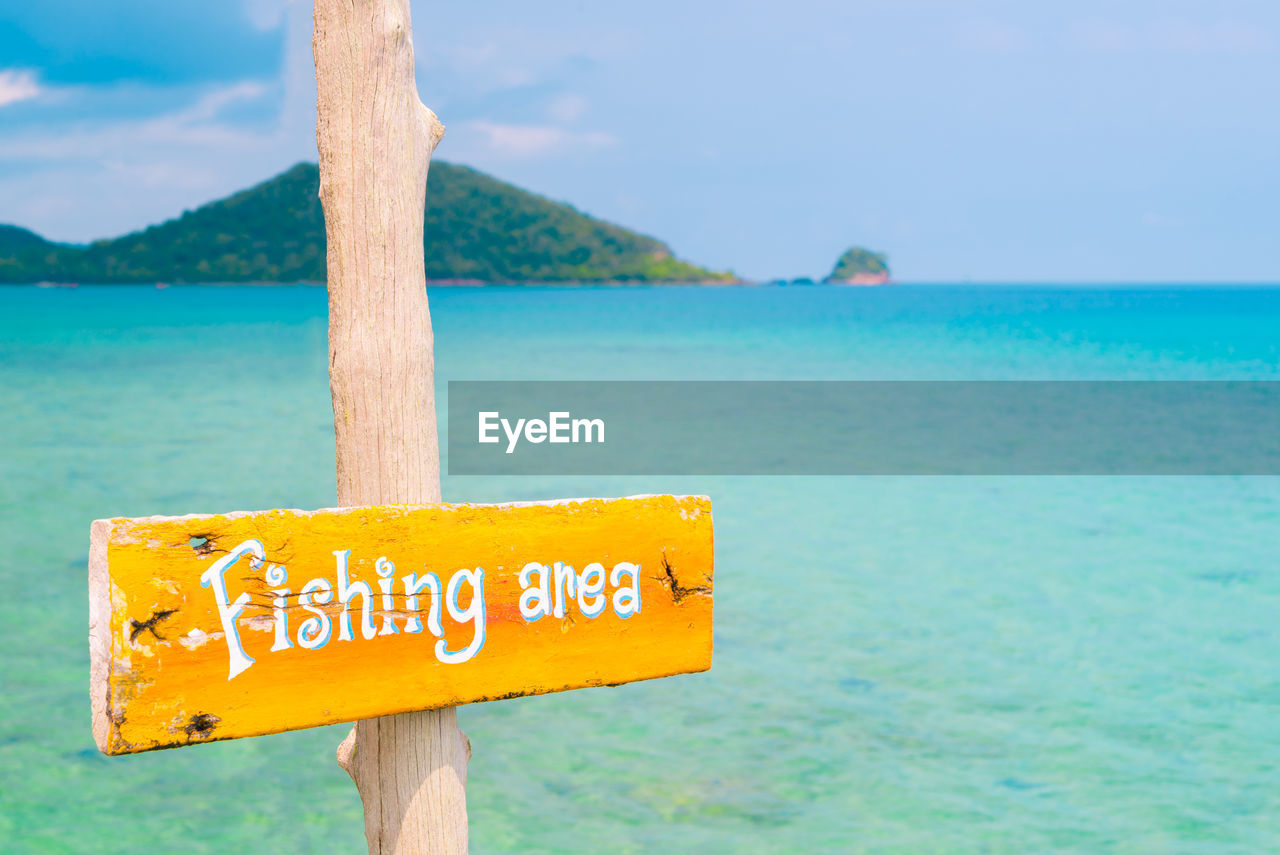 Information sign by sea against sky