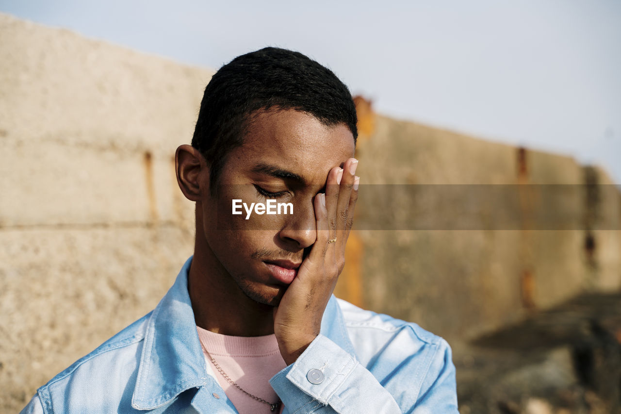 Man with head in hands and eyes closed standing outdoors