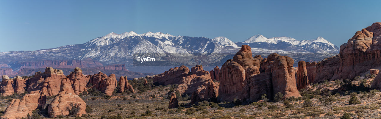 Panoramic view of sandstone rock formations against snow capped mountains on a sunny day