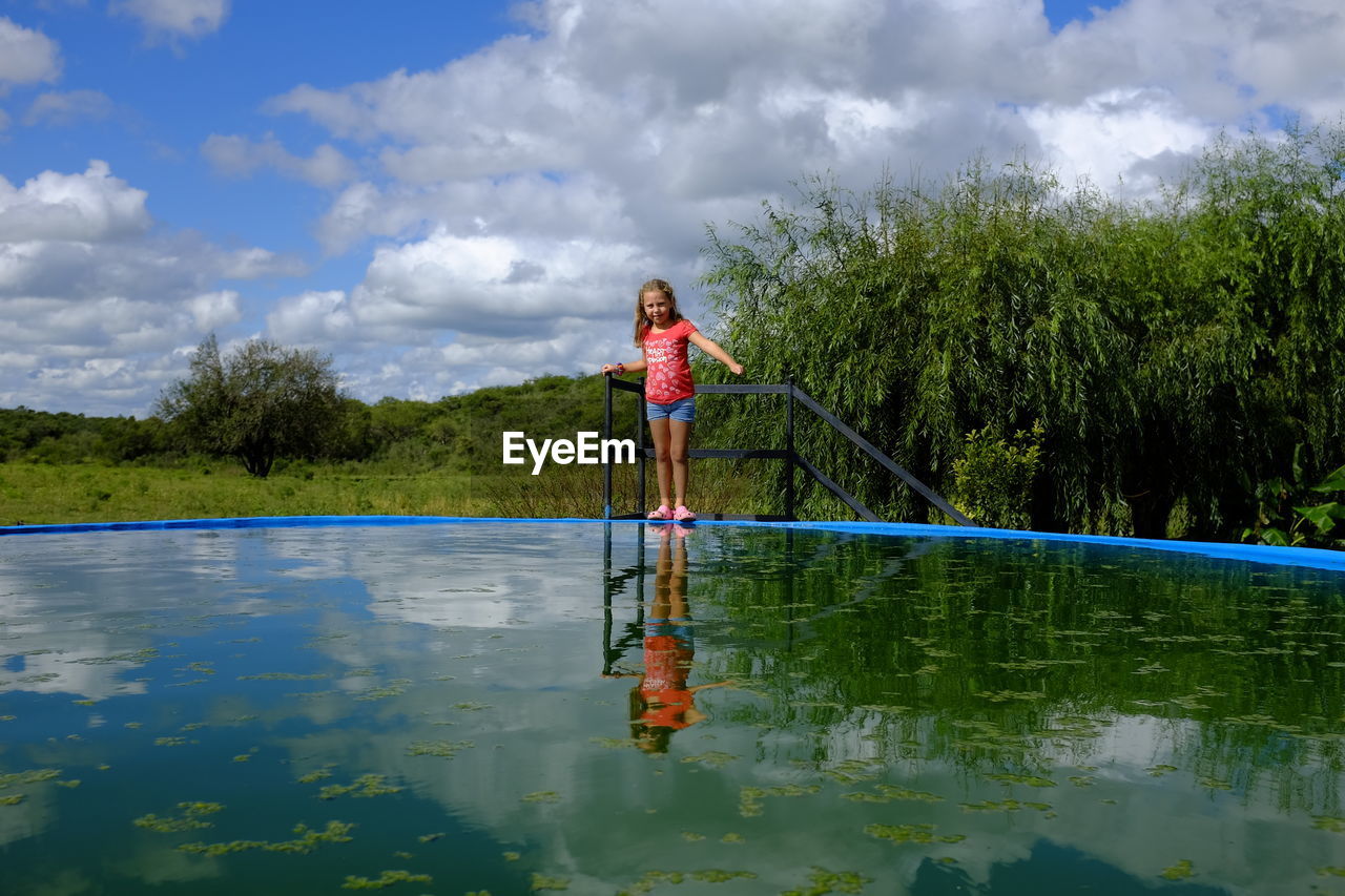 MAN STANDING BY LAKE AGAINST SKY