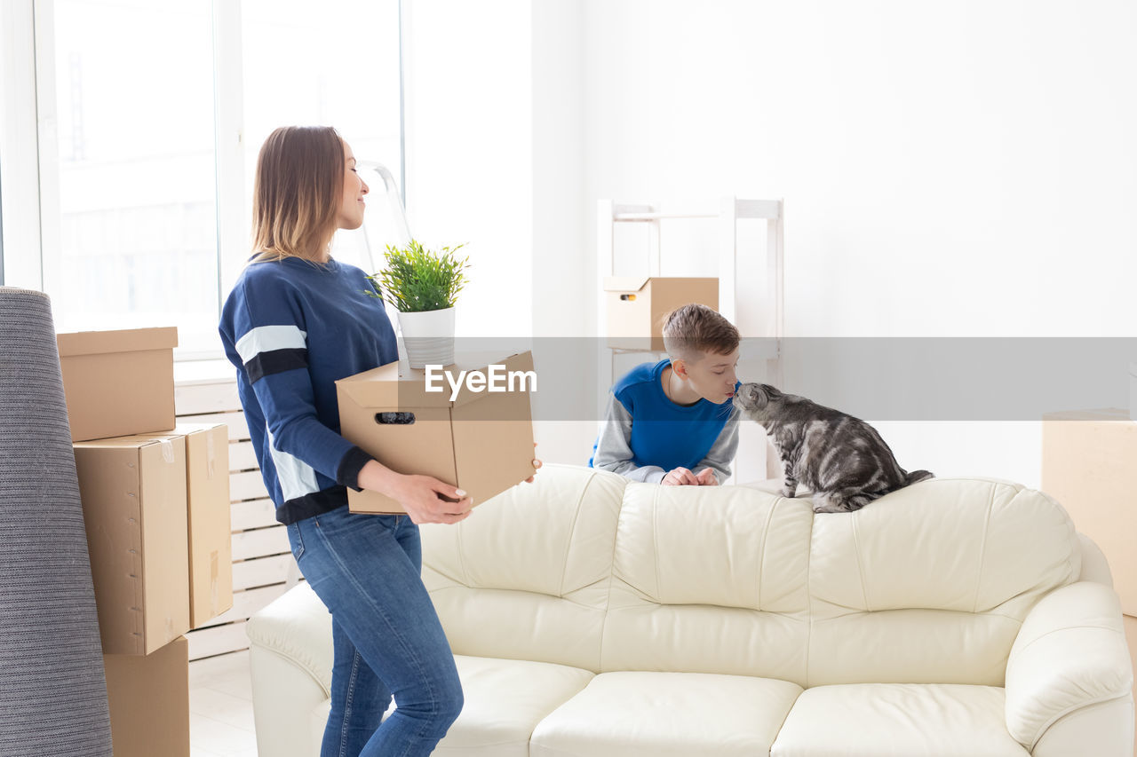 Mother carrying boxes while son playing with cat at home