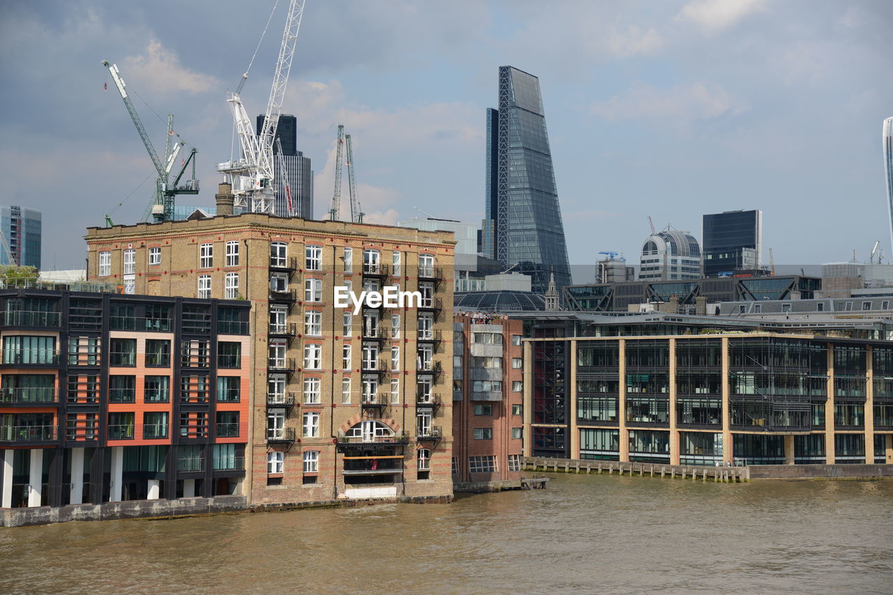 MODERN BUILDINGS BY RIVER AGAINST SKY