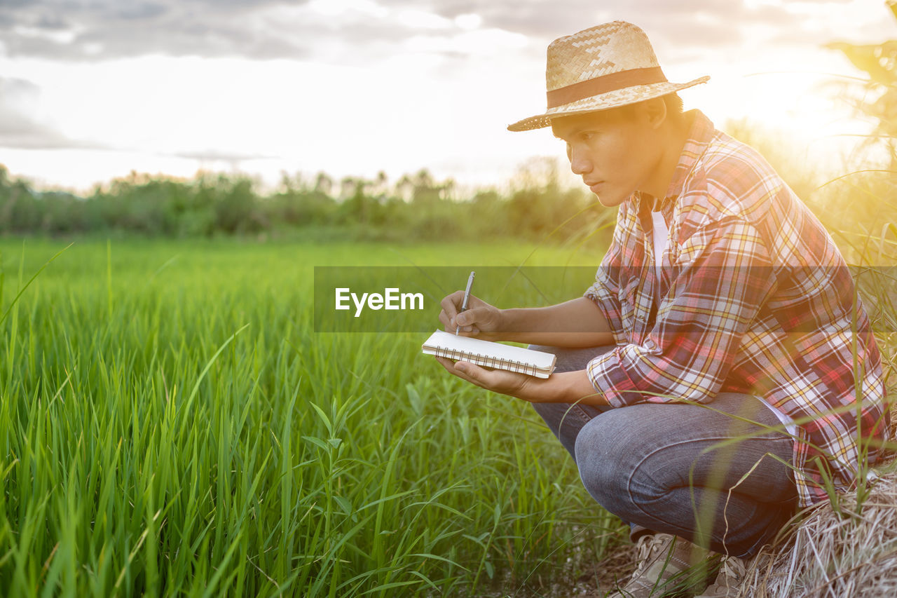 Man writing in book while examining plants on agricultural field