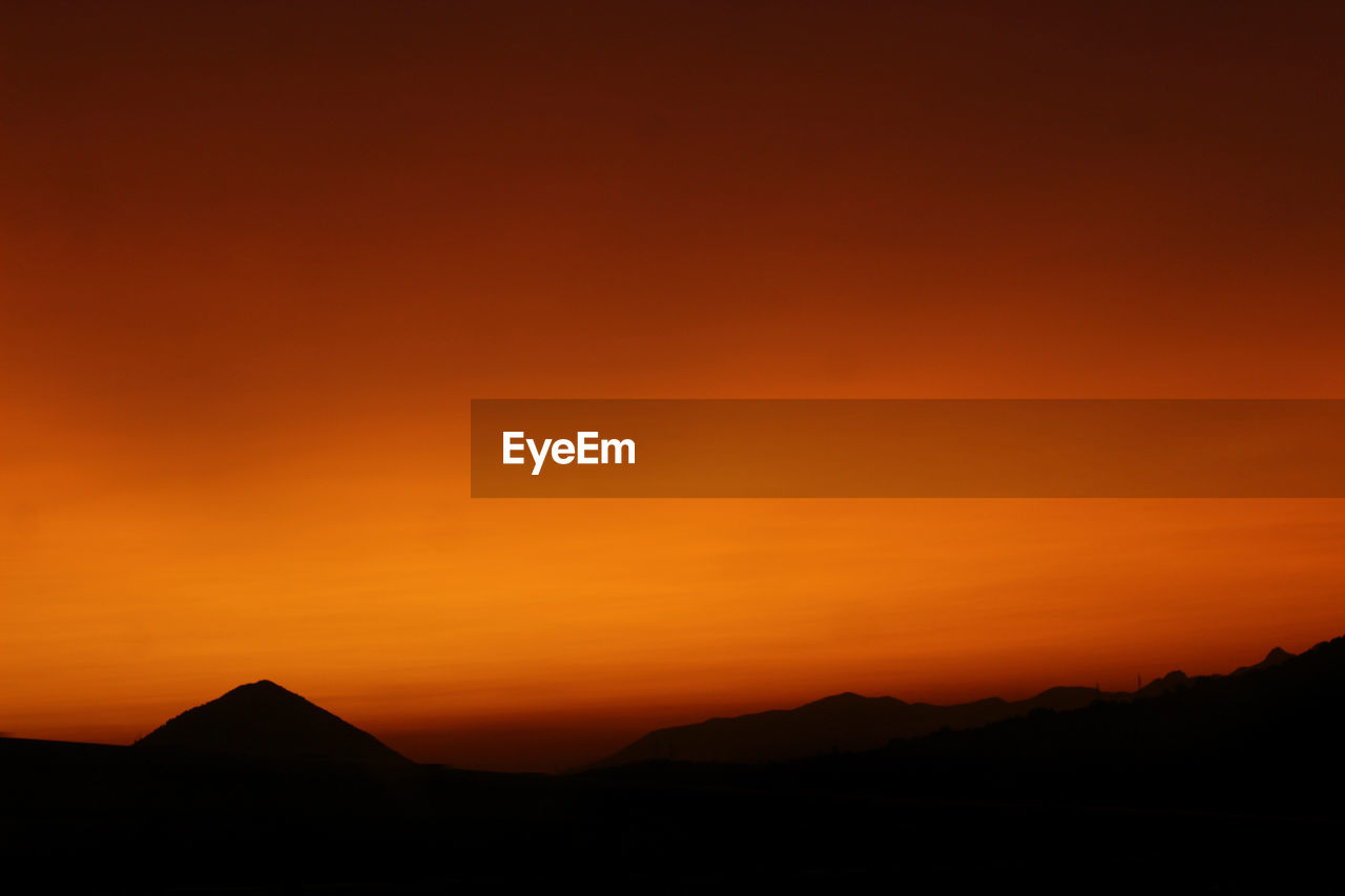 Scenic view of silhouette mountains against orange sky