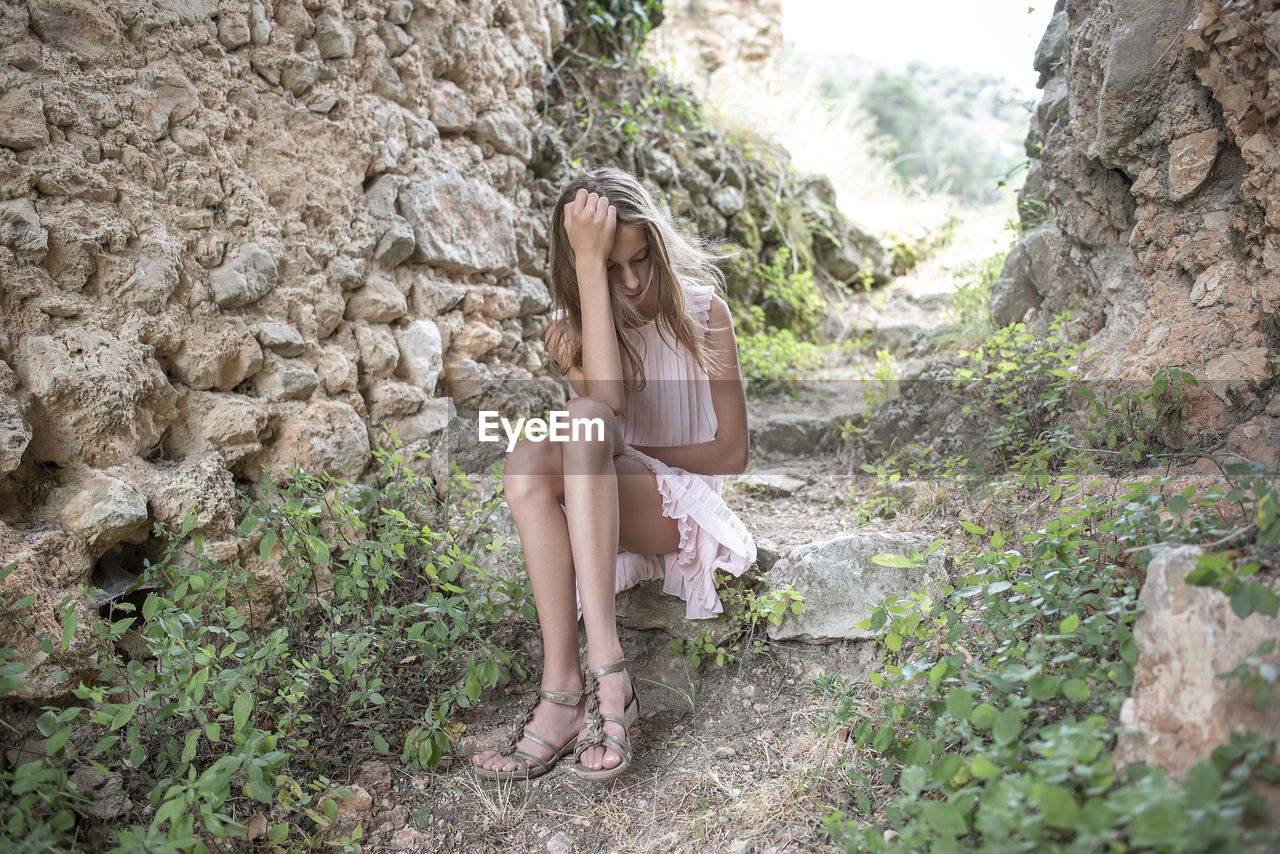 Full length of girl sitting on rock in forest