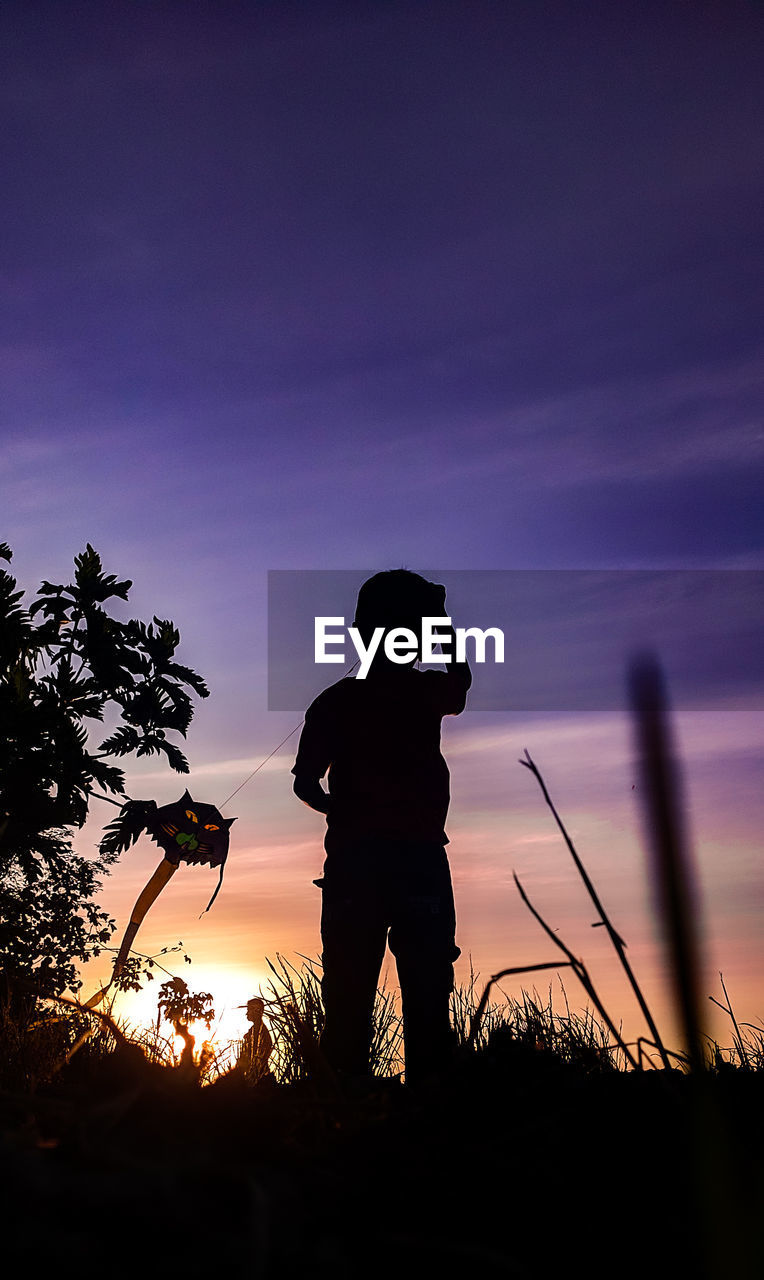 SILHOUETTE MAN STANDING ON FIELD AGAINST SUNSET SKY
