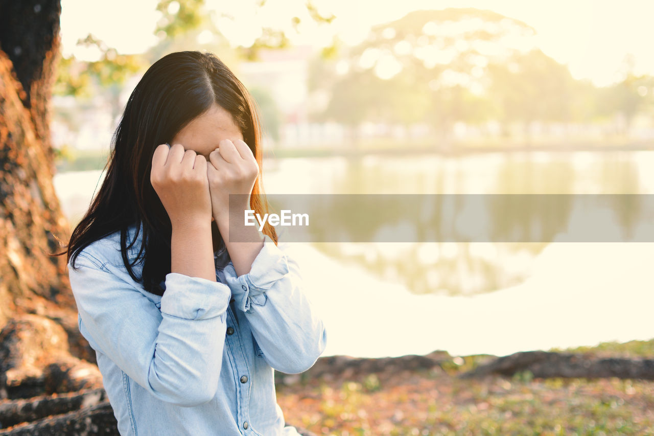 Woman covering face with fists by lake