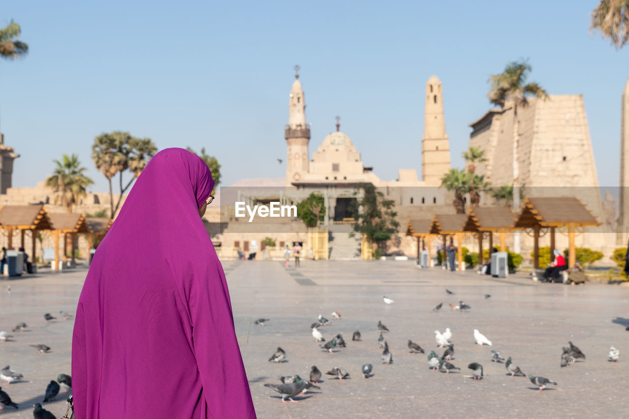 Unrecognizable muslim woman with veils walking through a typical square of her city with traditional