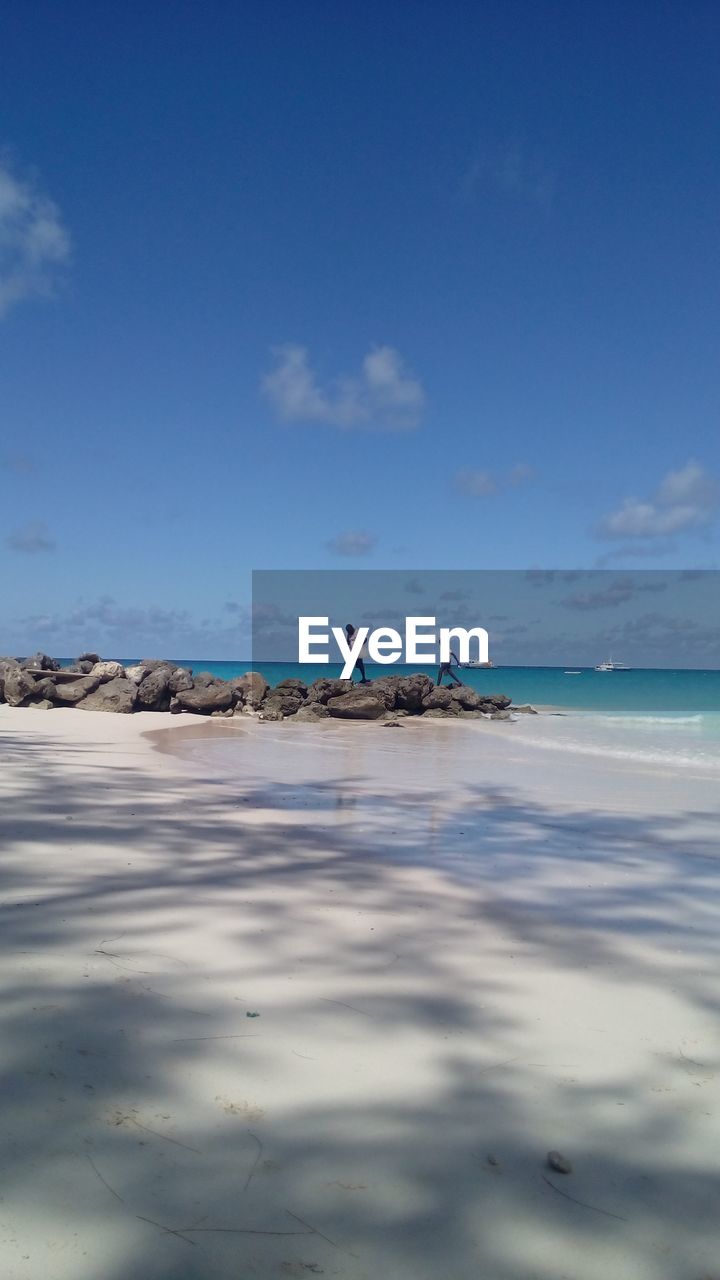 Distant view of men walking at beach against blue sky