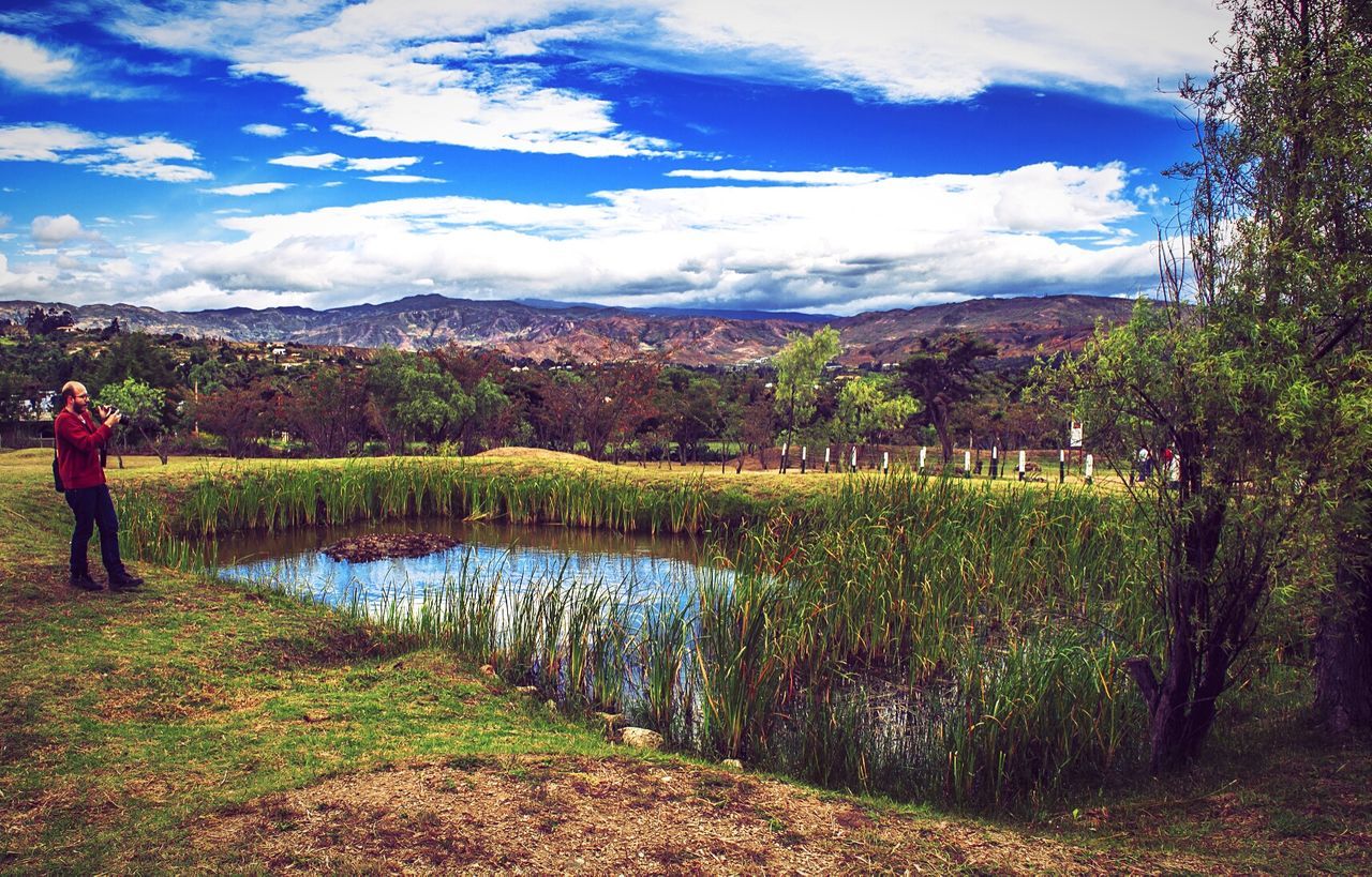 Full length of man standing near pond by mountains against sky