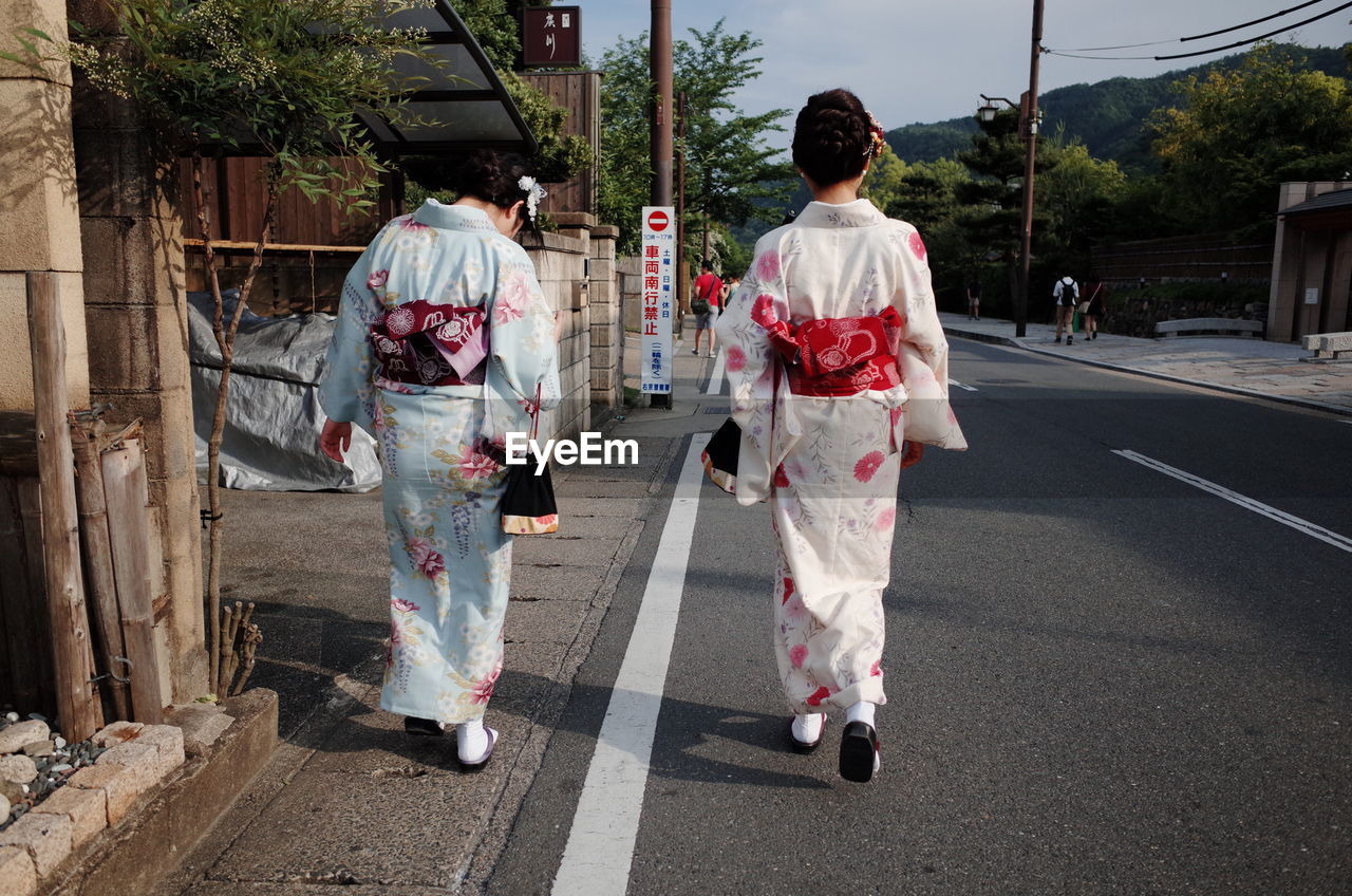 Rear view of geisha walking on road against cloudy sky