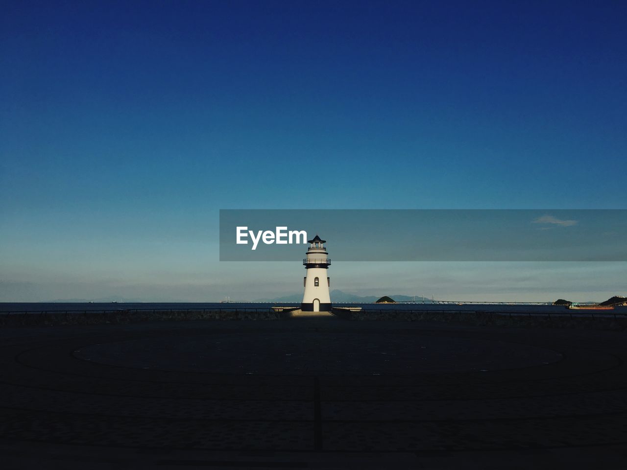 Lighthouse by sea against clear blue sky