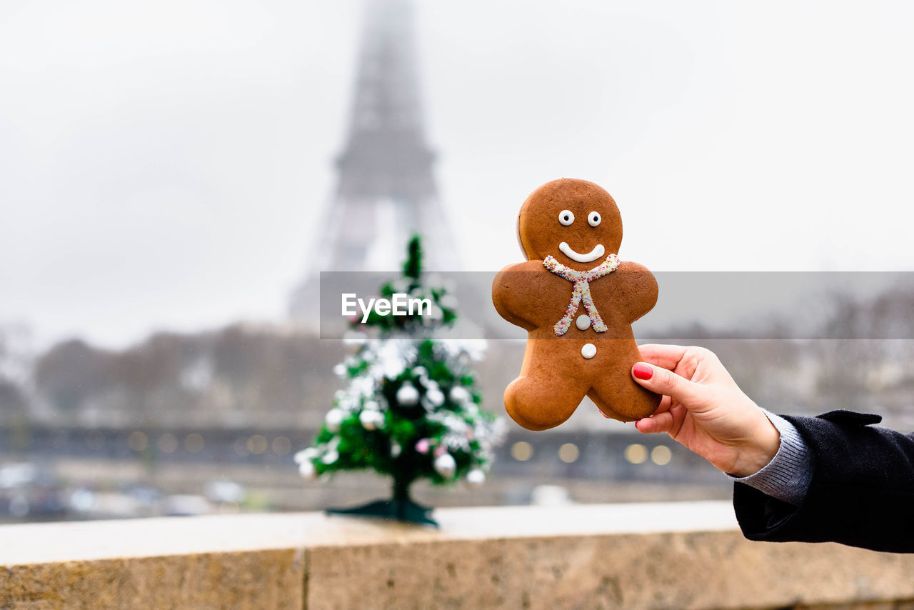 Cropped hand of woman holding gingerbread cookie against building