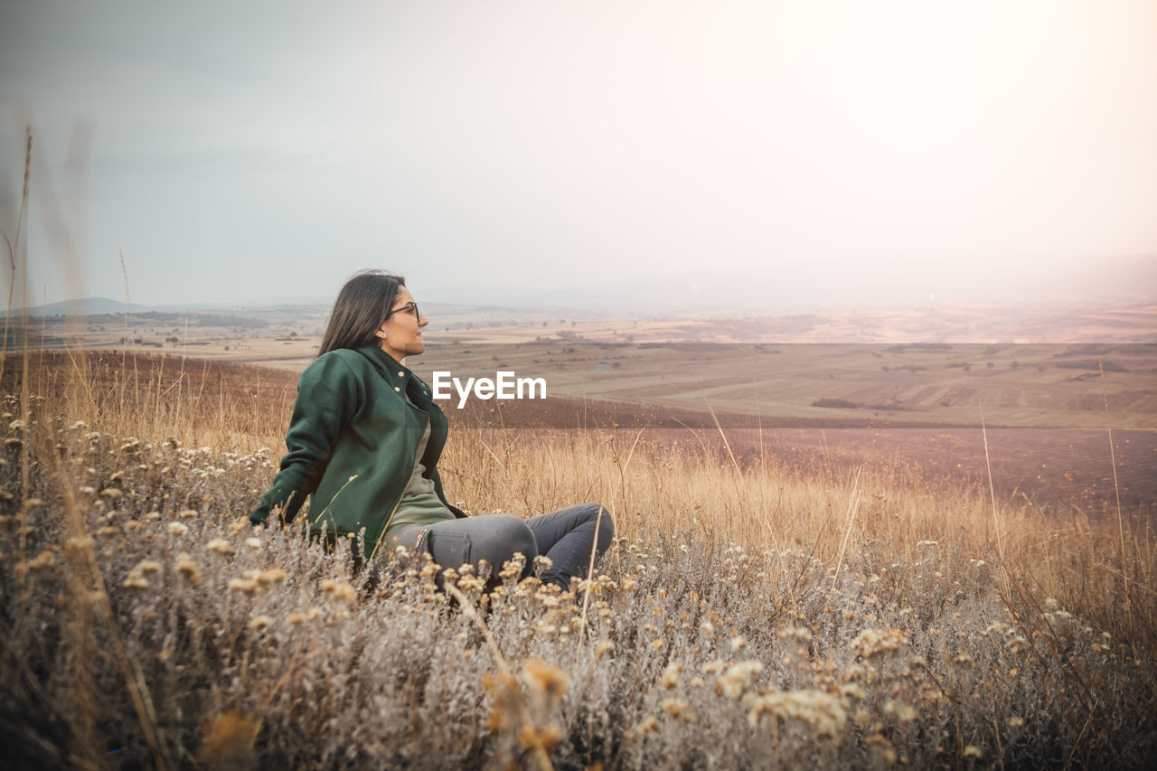 Young woman sitting on field against sky