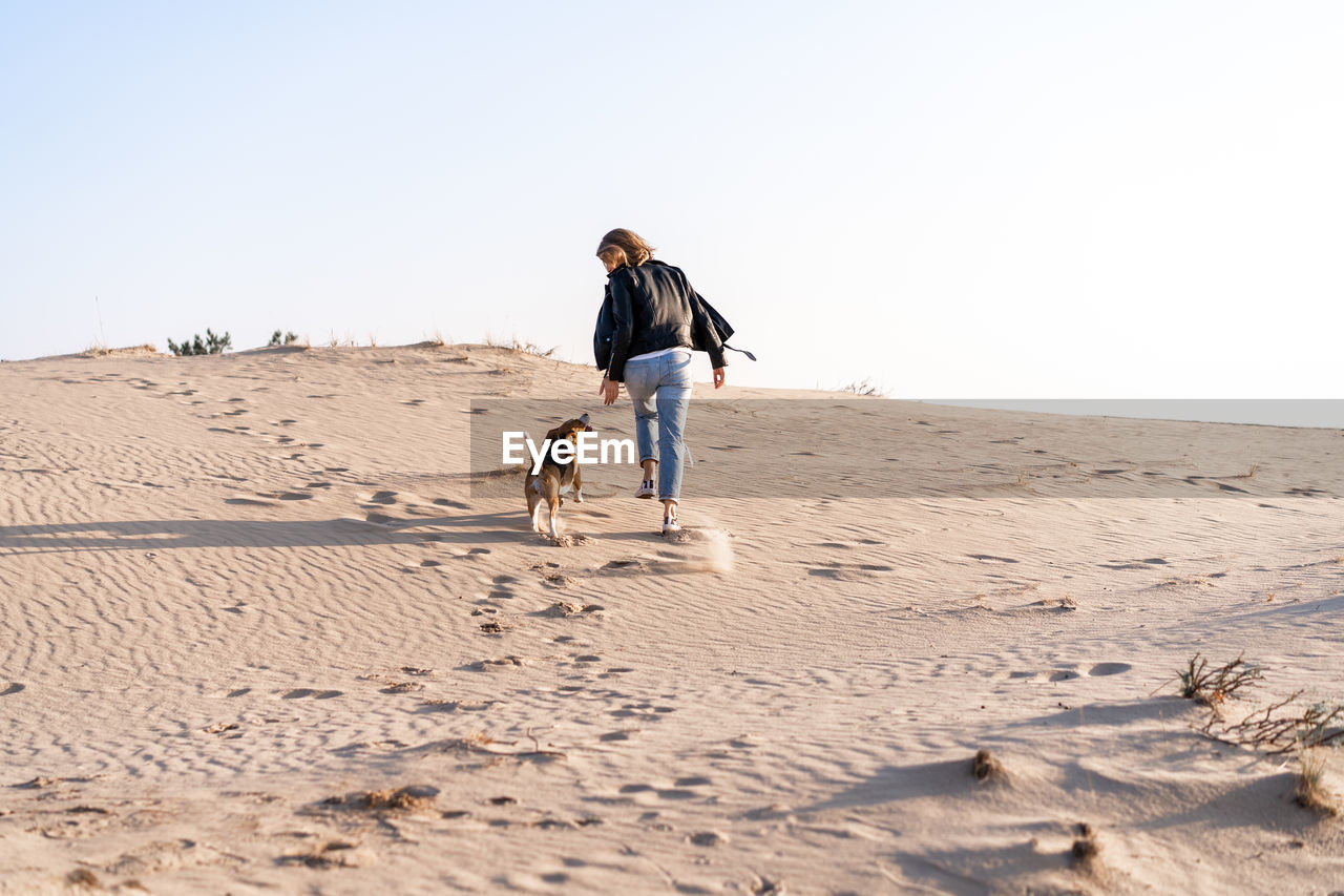 Rear view of woman with dog walking at beach