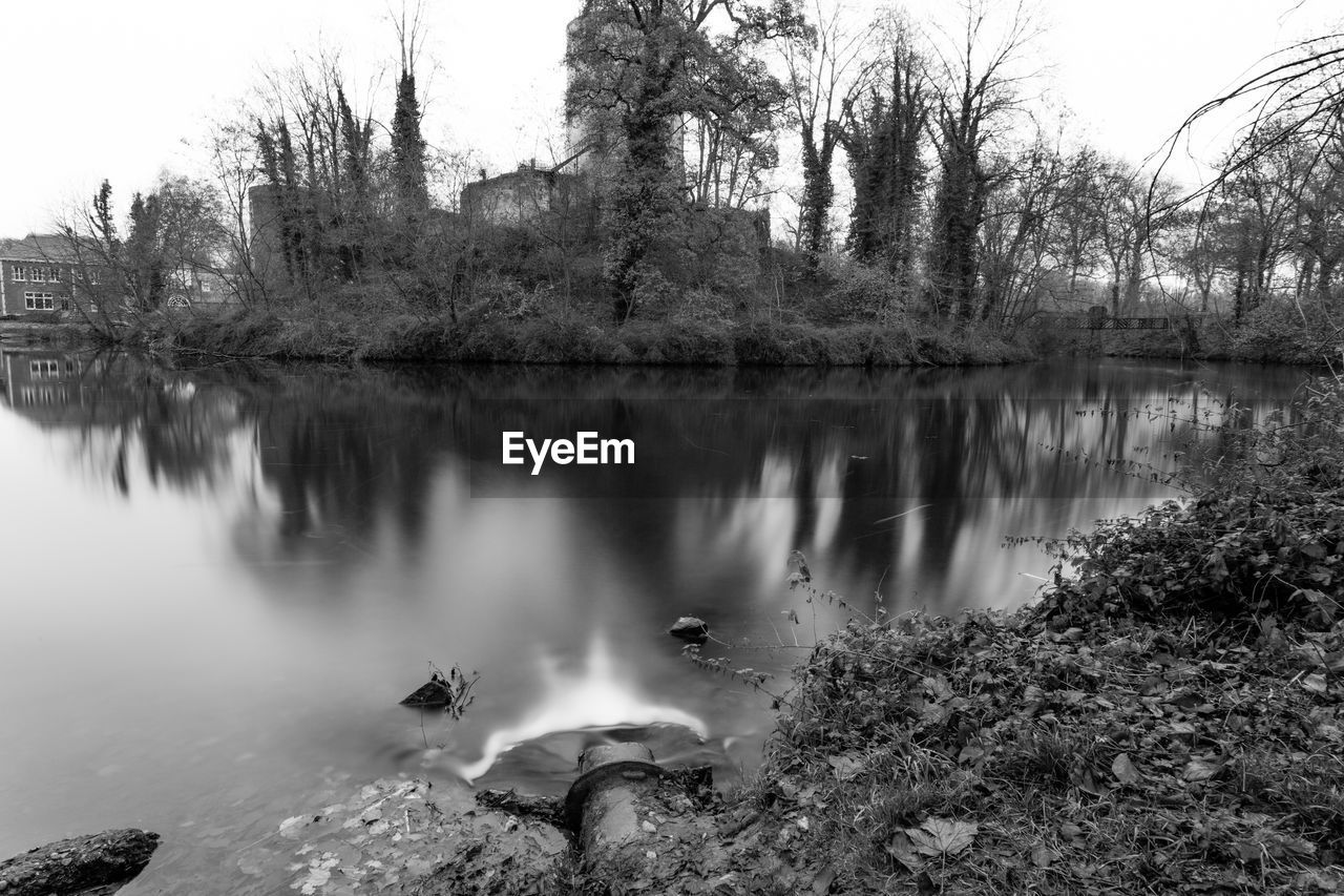 Pond with a metal drain pipe, water flowing into the lake, stein castle ruins in the background