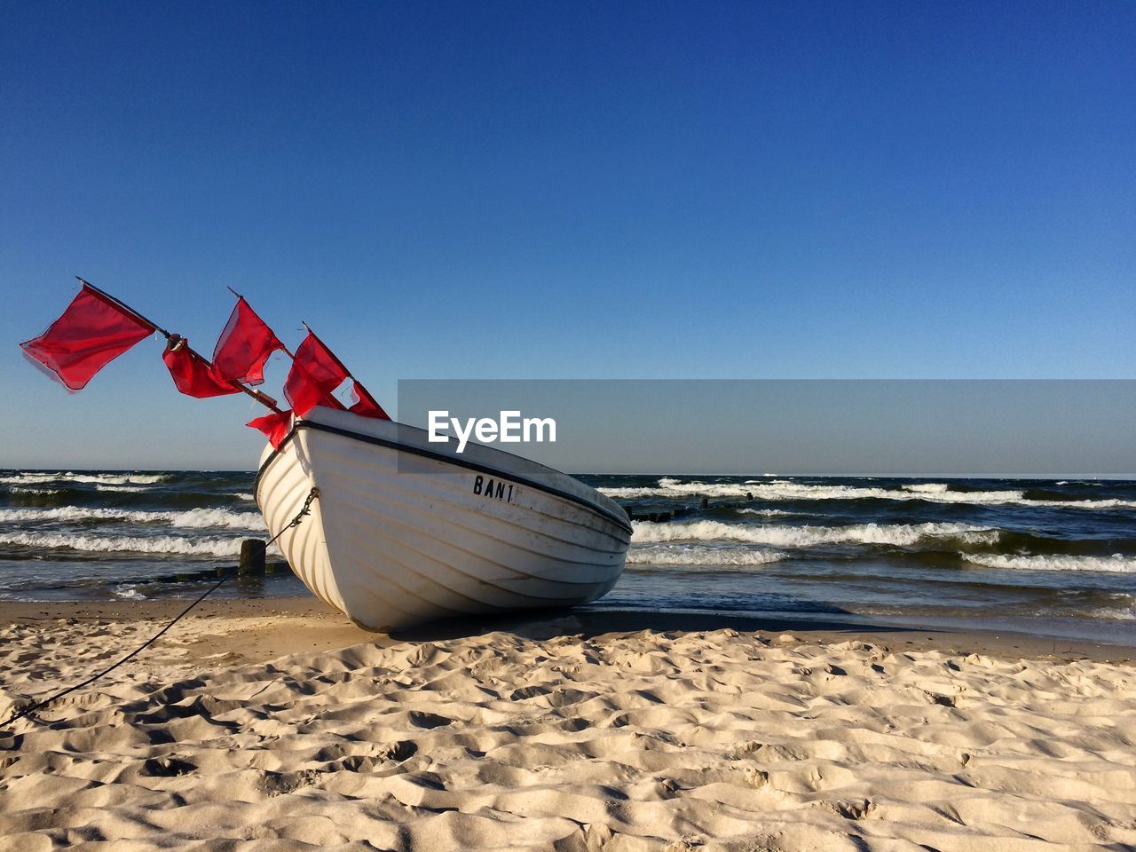 Boat moored at beach against clear blue sky