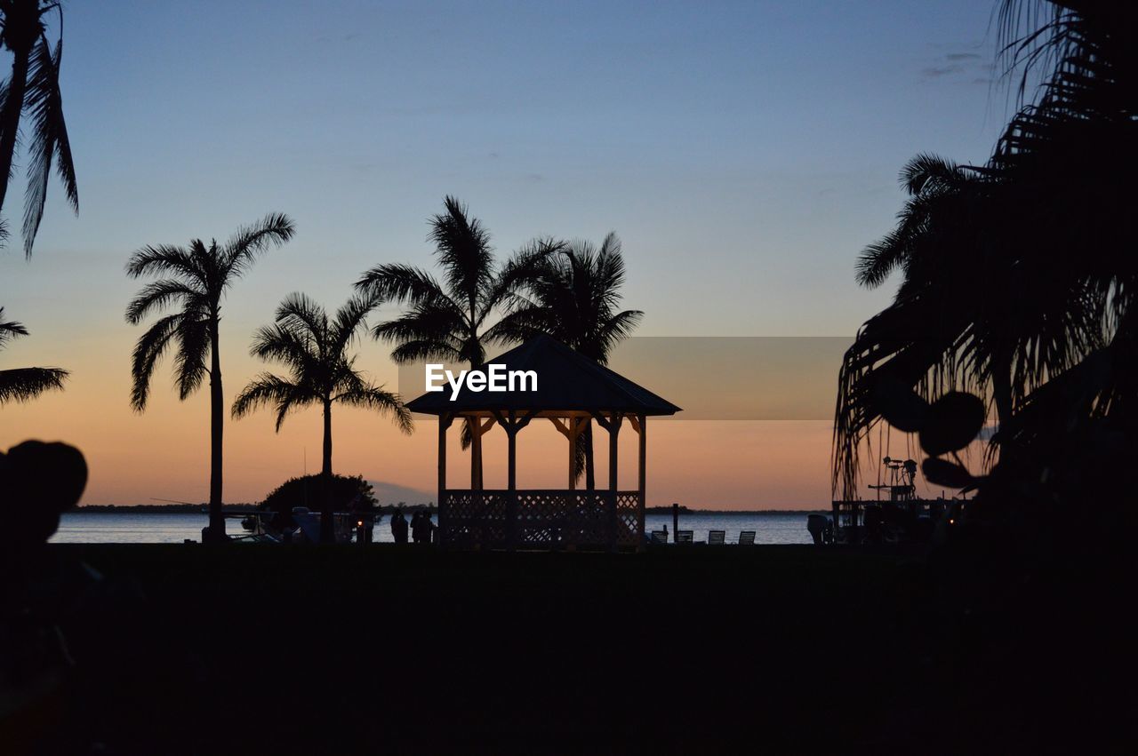 SILHOUETTE PEOPLE BY SWIMMING POOL AT SUNSET