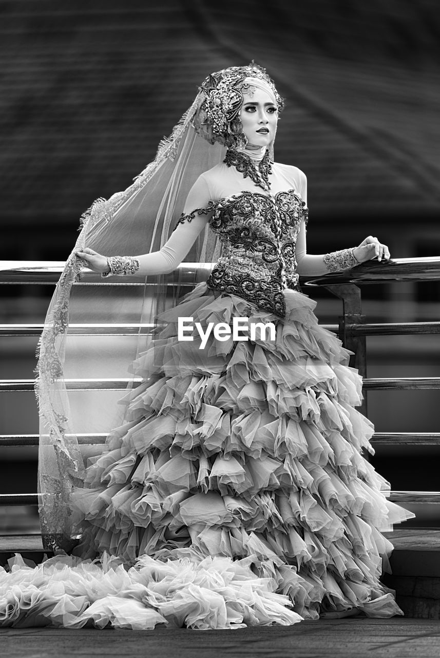 Young woman in dress standing on footpath by railing