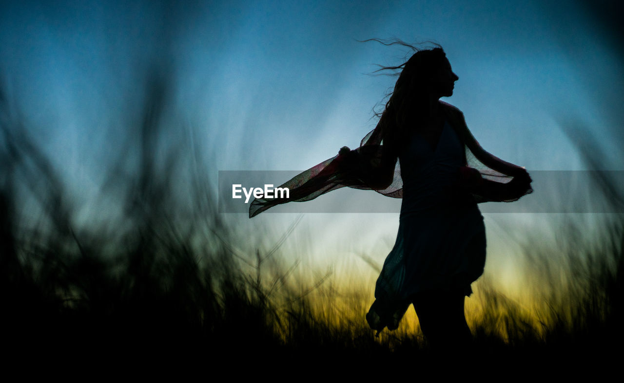 Silhouette woman standing on field against sky during sunset