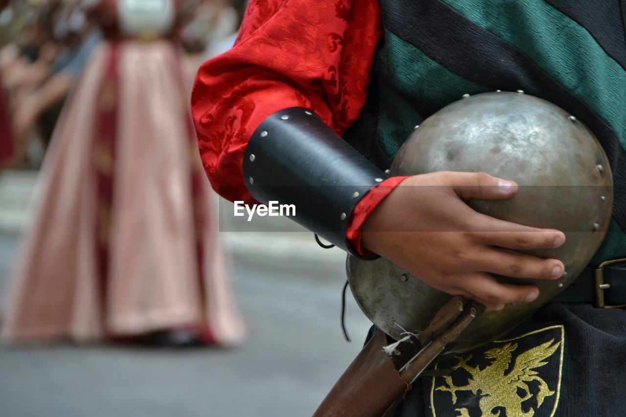 Midsection of person in costume holding armor outdoors