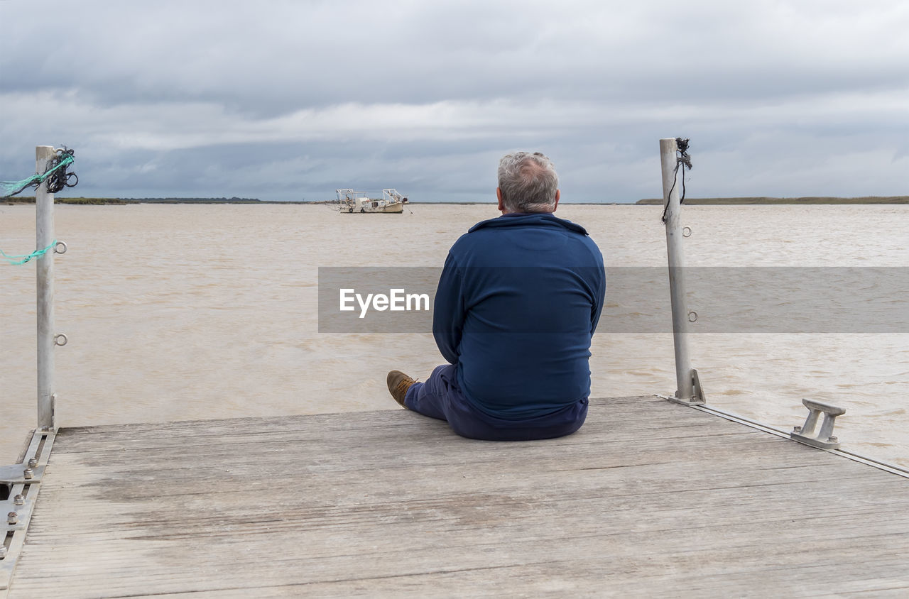 rear view of man sitting on beach against sky