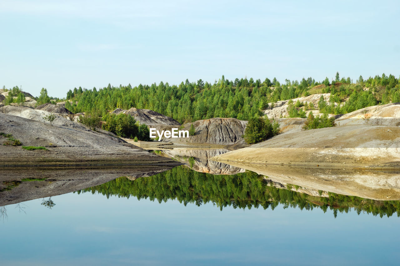 View on a flooded quarry with blue water and reflection of hills and forest.