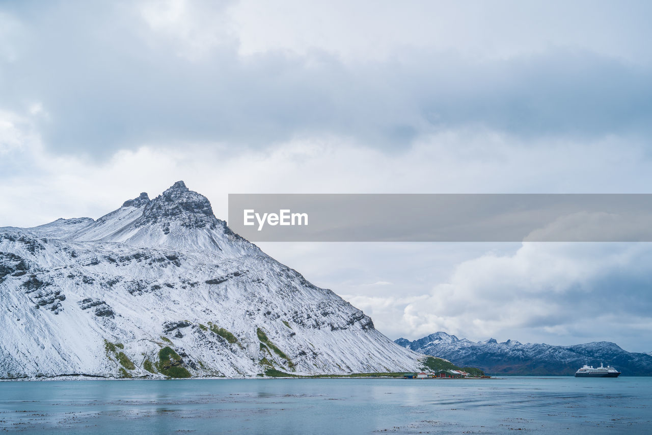 Scenic view of sea by mountain against sky