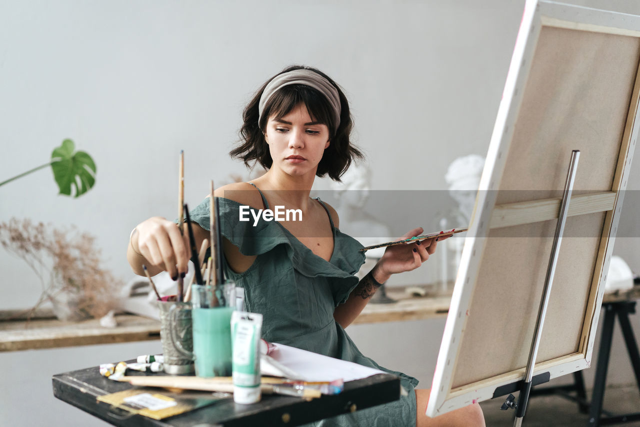 Young woman painting on canvas while sitting on table