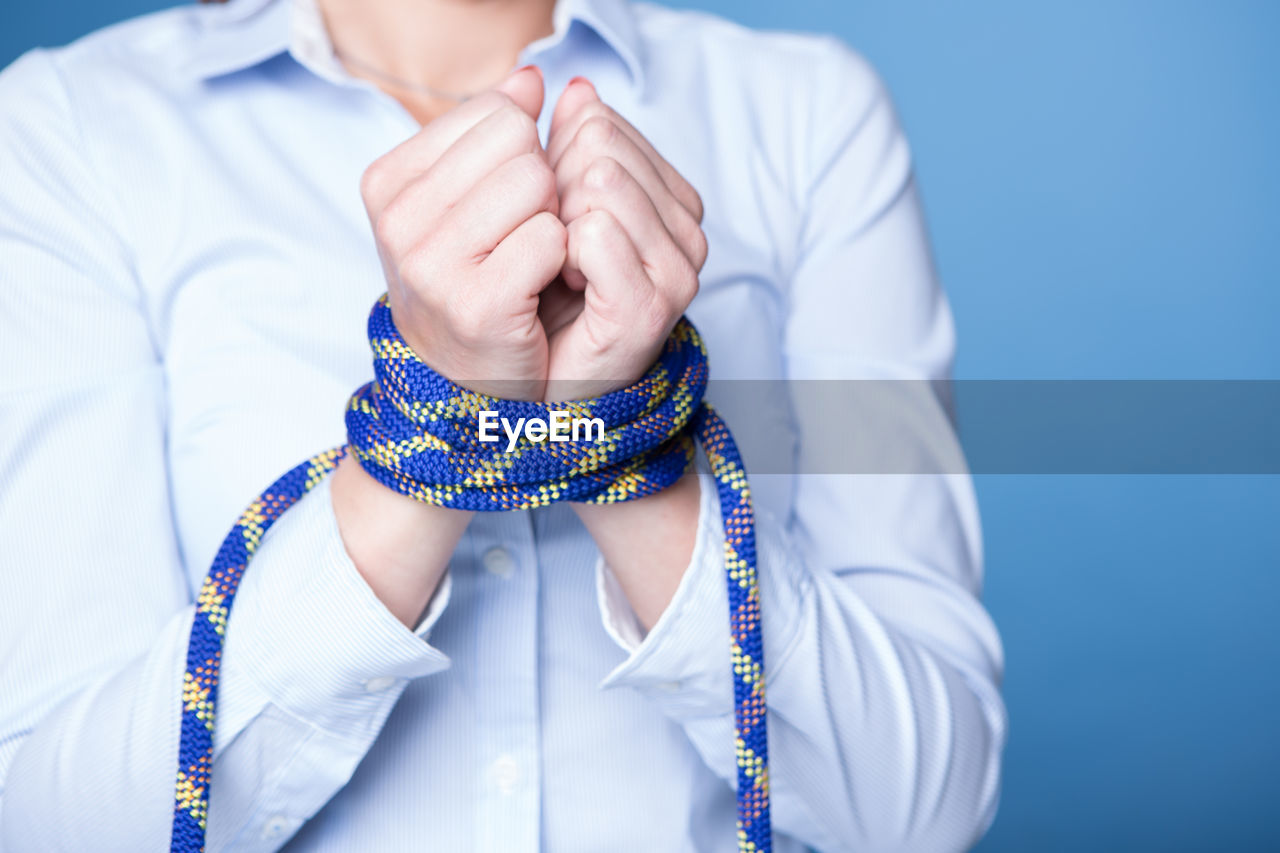 Midsection of businesswoman with hands tied over blue background
