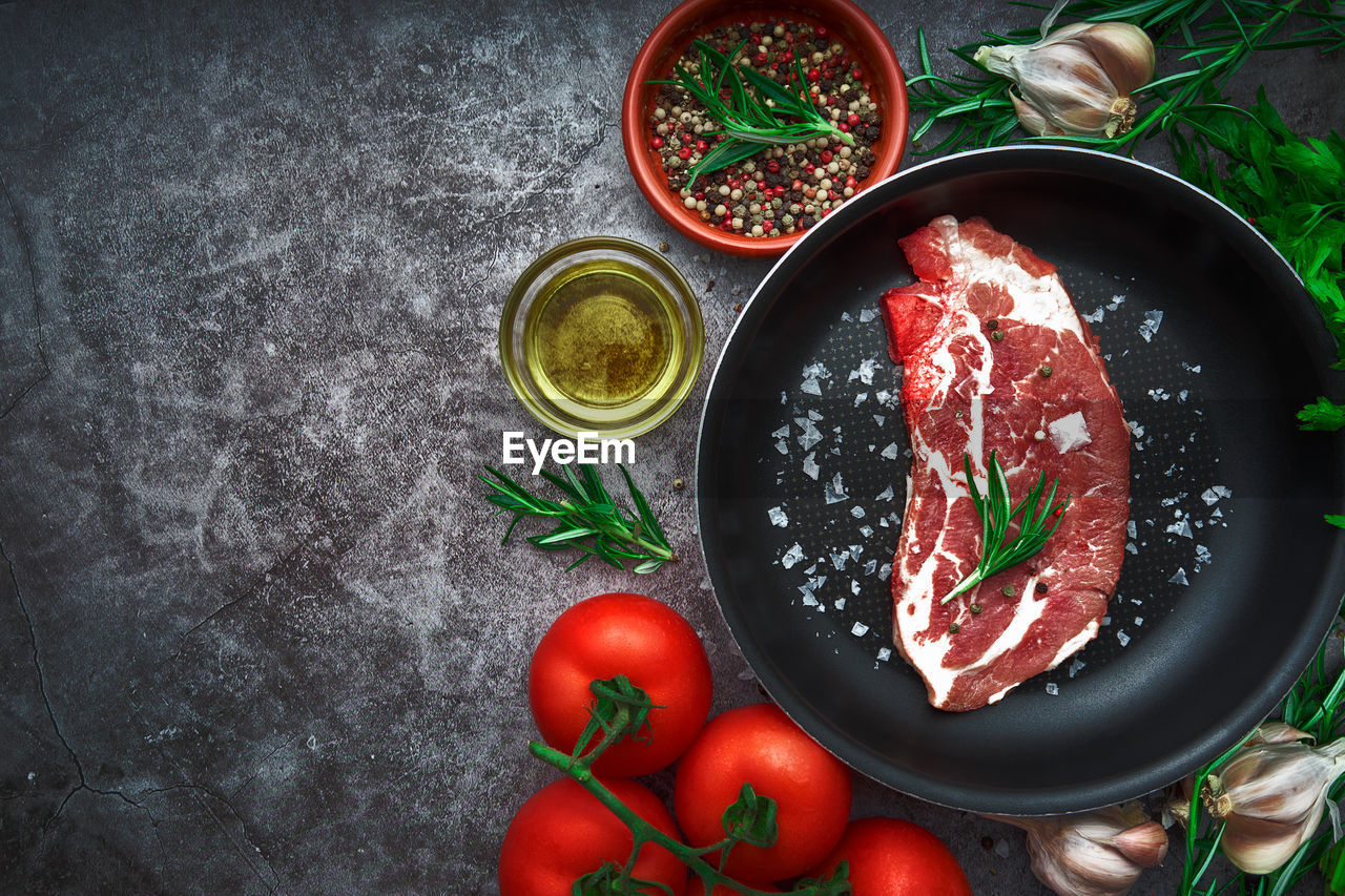 Raw beef steak with tomato, garlic, pepper, salt and rosemary on frying pan on a dark background.