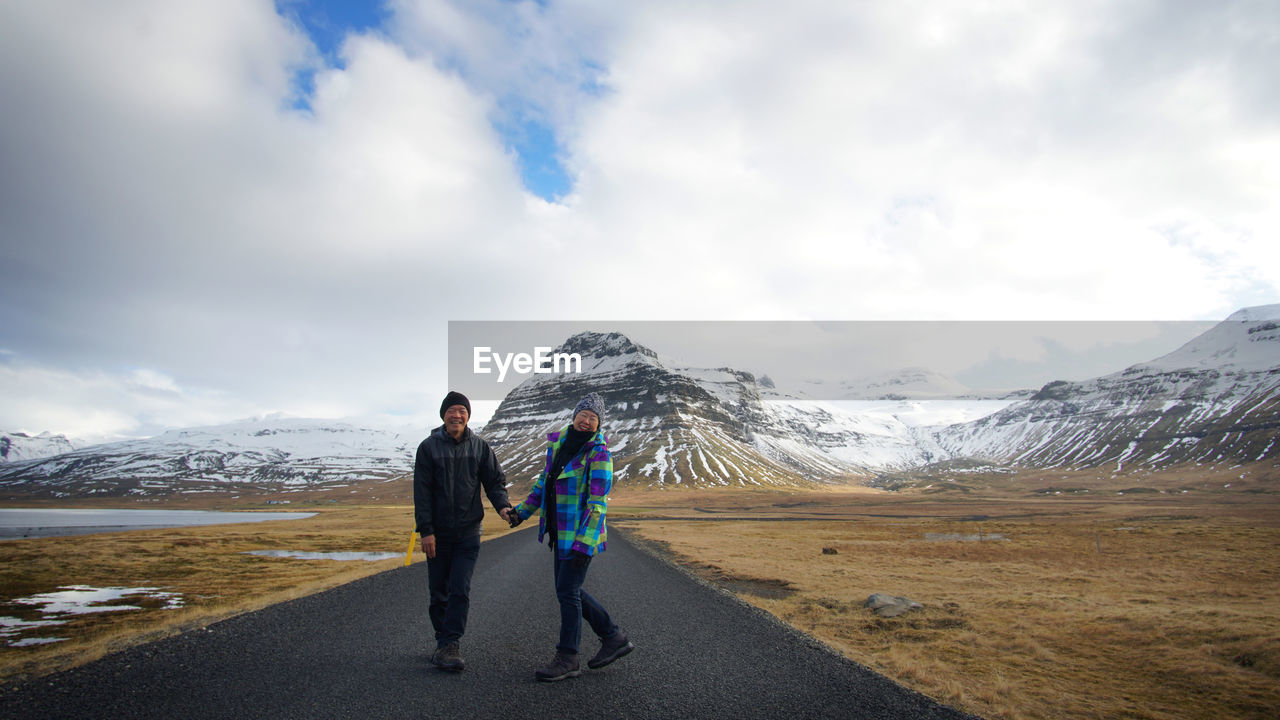 Full length of couple standing on road against cloudy sky