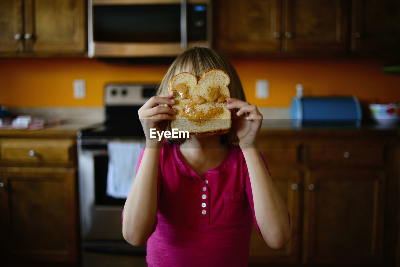 Girl holding bread against her face in kitchen