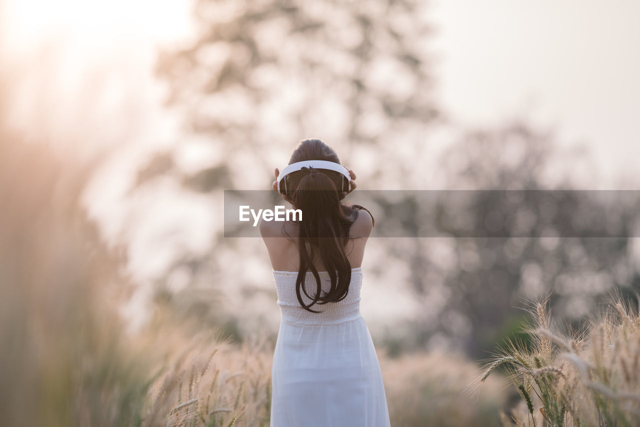 Rear view of woman using headphones while listening music on field during sunset