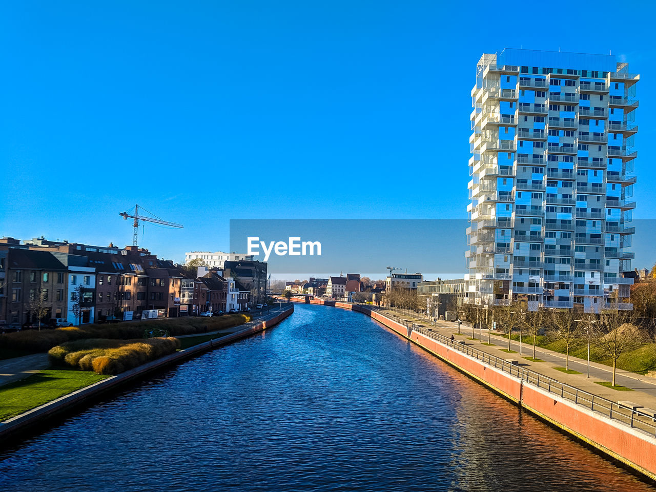 Canal amidst buildings in city against clear blue sky