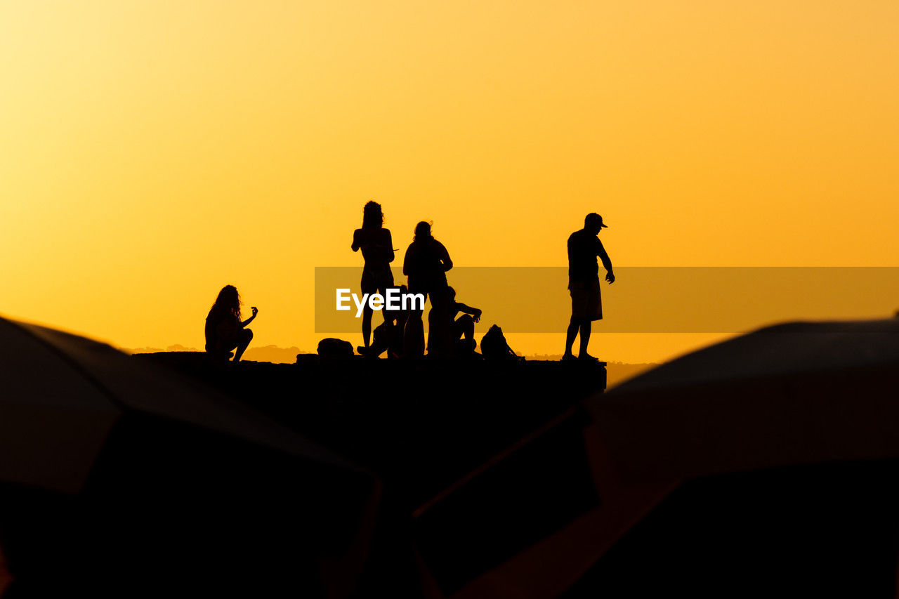 Group of people, in silhouette, are seen on the pier of porto da barra against the sunset 
