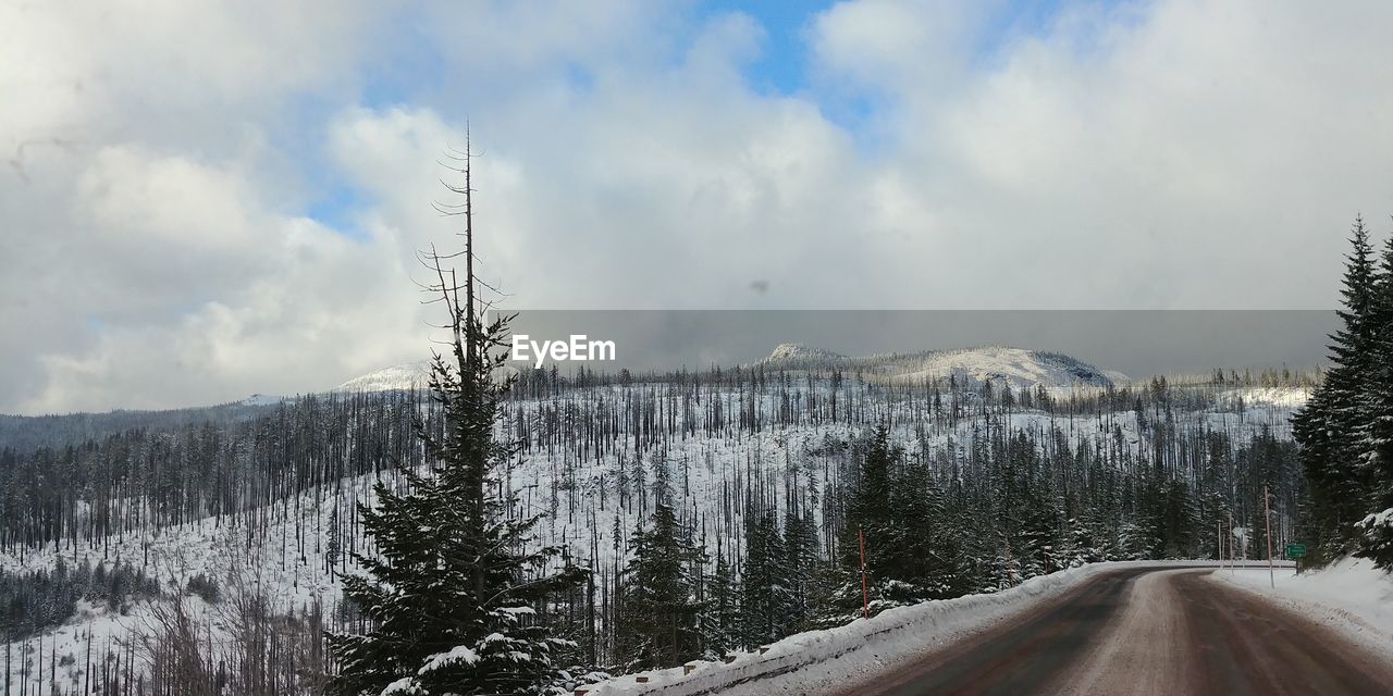 Road by snow covered landscape against sky