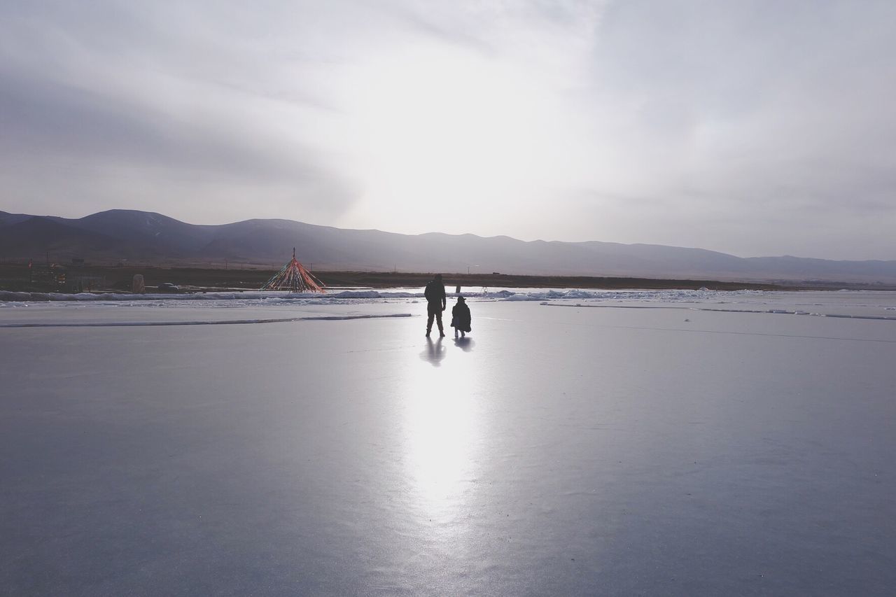 Rear view of parent with child walking on frozen lake against sky