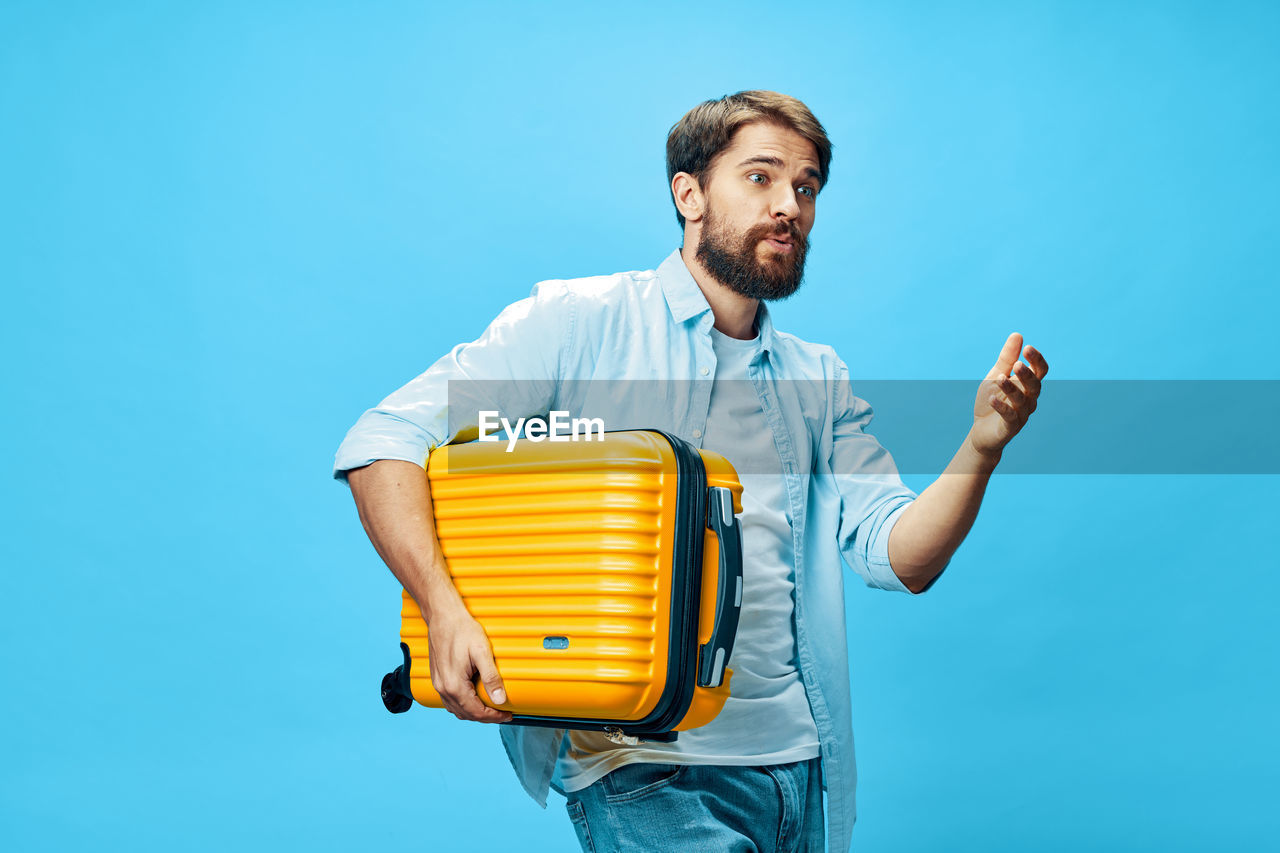 Young man holding suitcase against colored background
