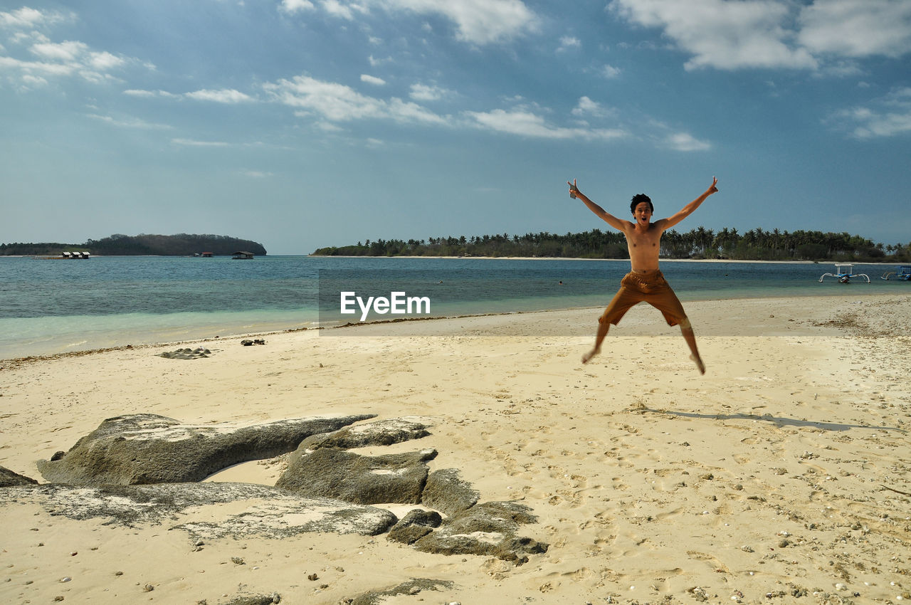 Shirtless man jumping over beach against sky