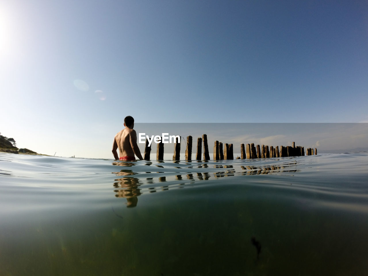 Water surface shot of shirtless man wading in sea against sky